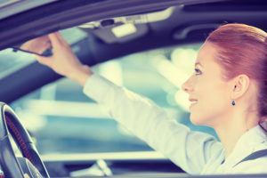 A woman adjusting her mirror, practicing safe driving habits on the road.