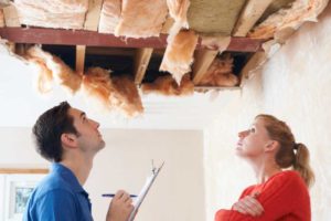 A woman looking at her damaged home's ceiling and an insurance adjuster writing on a clipboard