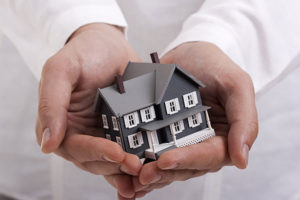 Hands holding a model house representing protection