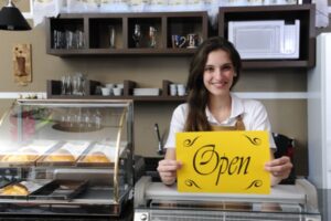 A business owner holding an Open sign at the register of her business
