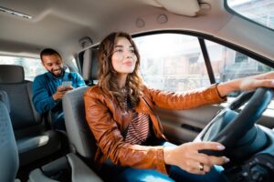 A woman driving a personal rideshare vehicle with a man in the rear seat, protected by insurance for rideshare